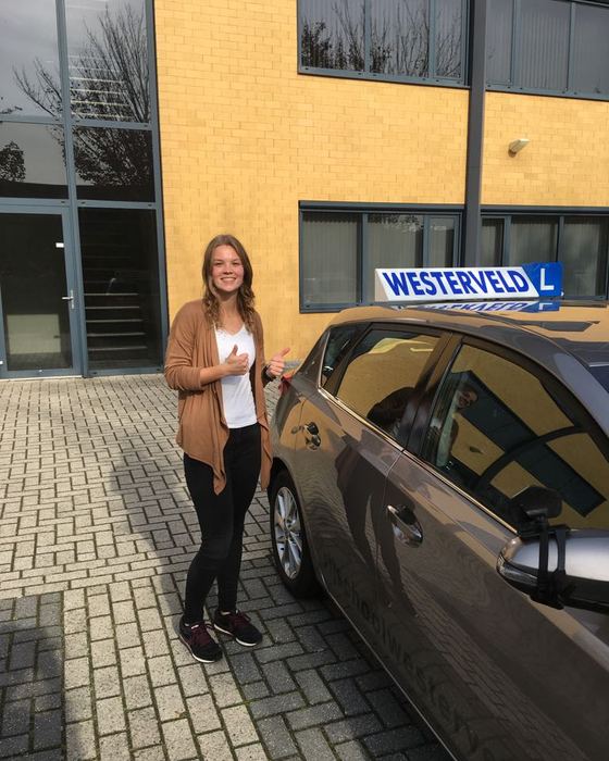 Esmee Molenbuur uit Diever naast de lesauto na haar geslaagde examen