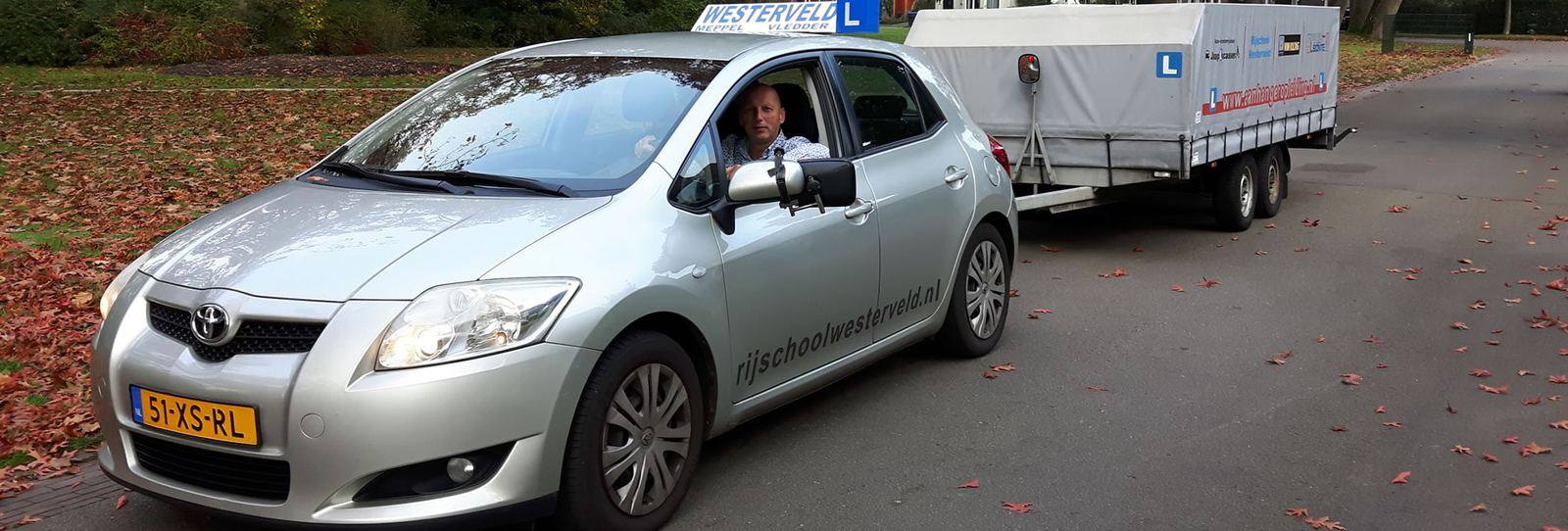 Instructeur van Rijschool Westerveld in de lesauto met aanhangwagen