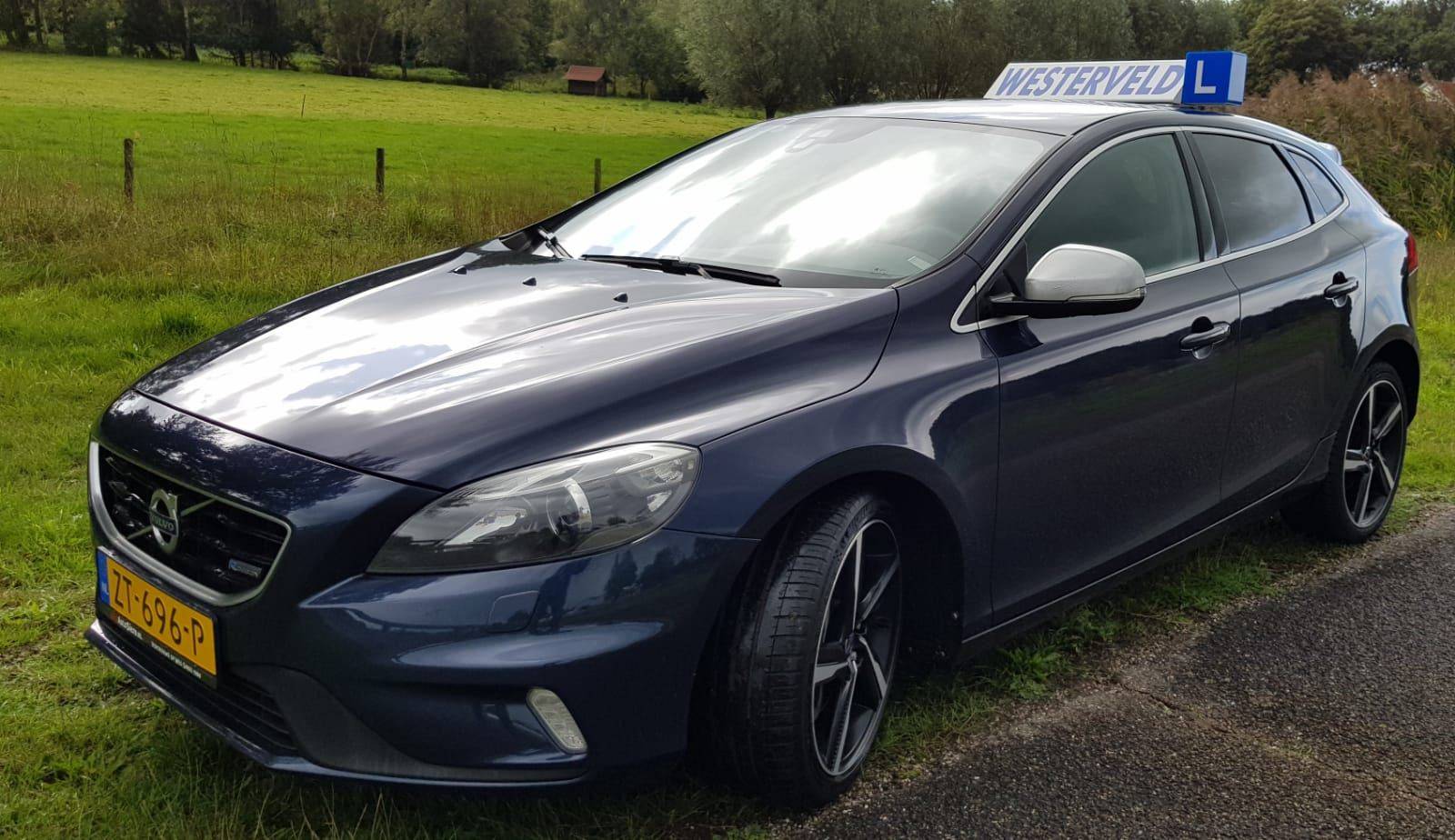 De lesauto van Rijschool Westerveld, een donkerblauwe Volvo V40 met lesbord, aan de rand van Meppel